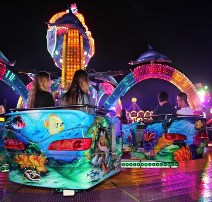 Colourful bumper car ride with lights of other rides in the background.